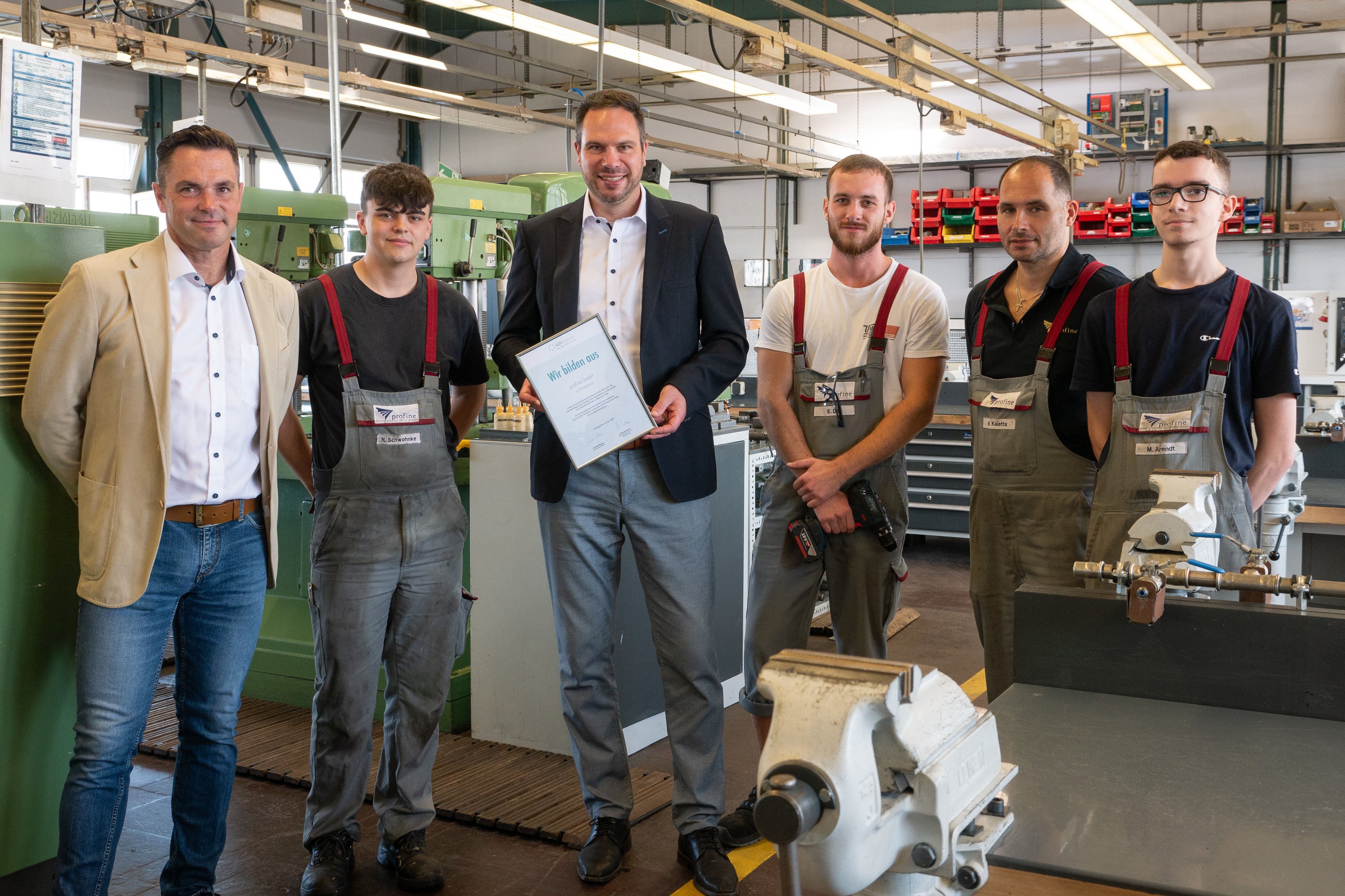 Stefan Britz, HR Director (Mitte), und Andreas Langner, Ausbildungsleiter, mit einigen Auszubildenden und ihren Ausbildern in der Ausbildungswerkstatt bei profine. (Foto: Hasübert/Chemieverbände)